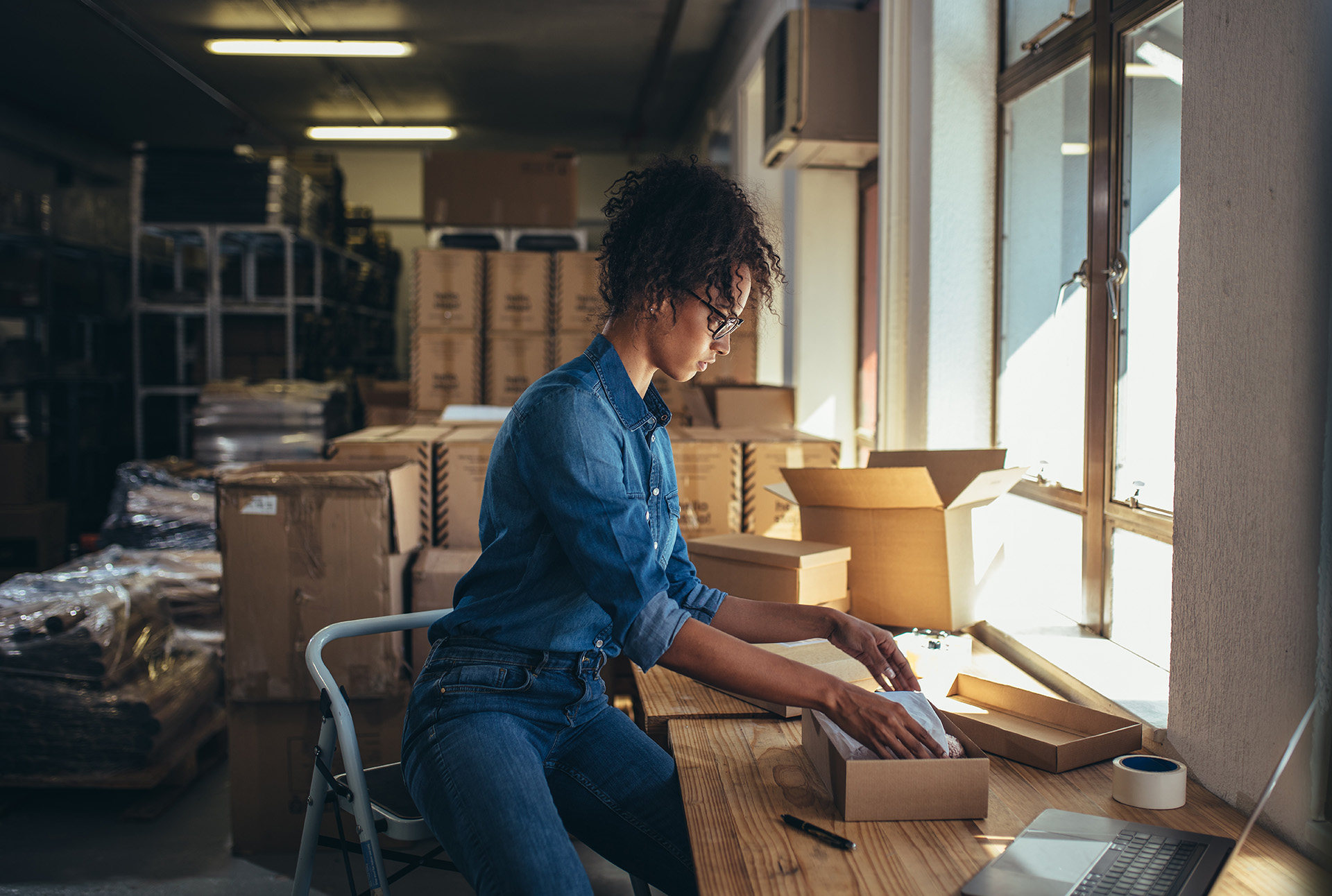 Female business owner packing orders into corrugated box for shipping to customer.