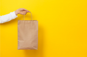 Person holding a paper bag on a yellow backdrop