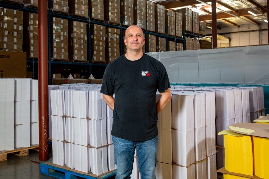 Wolfgang standing in front of pallets of envelopes getting manufactured