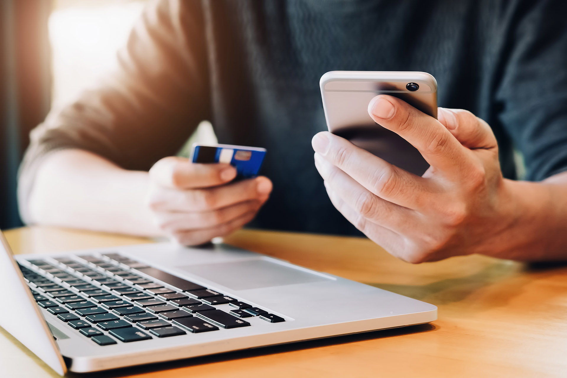 Person at a computer holding a phone and credit card making a payment online